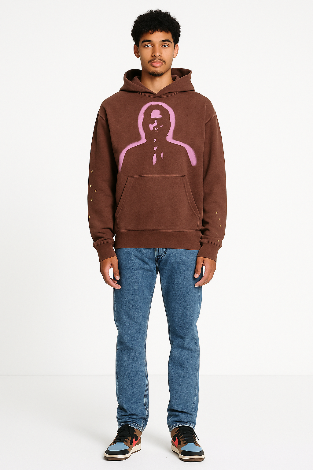Man wearing a brown hoodie with a pink graphic and blue jeans on a white background