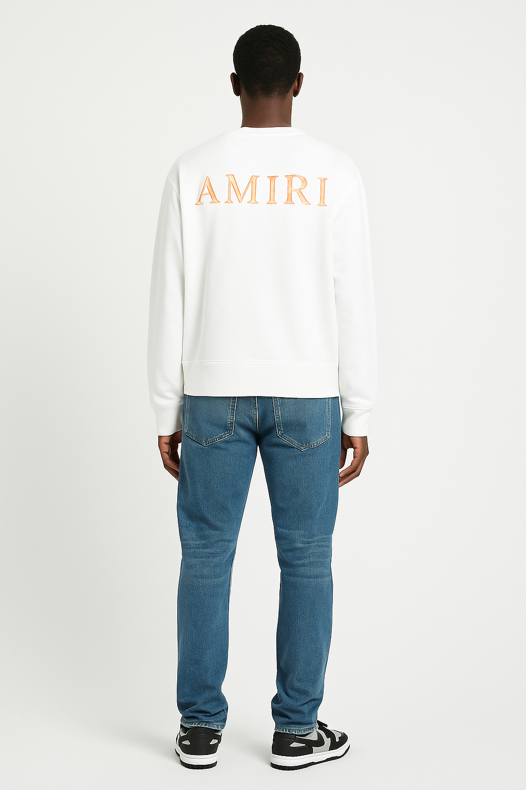 Person wearing a white 'AMIRI' sweatshirt and blue jeans on a white background